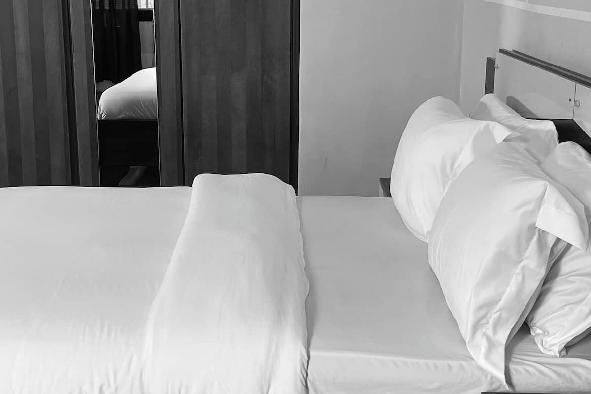 Una cama bien hecha con sábanas blancas en una habitación con suelo de madera y una puerta con cortinas.