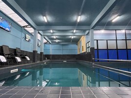 Una piscina interior con paredes de azulejos, luces en el techo y sillas de descanso a un lado.