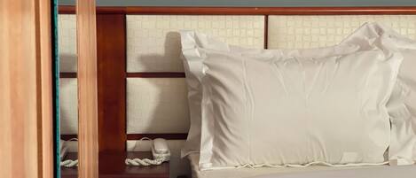 A hotel room with a bed, a wooden headboard, a nightstand with a telephone, and a wall-mounted light switch.