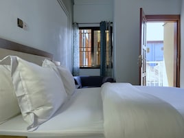 Una habitación de hotel con cama, una silla, un ventanal con cortinas y una puerta que da al exterior.