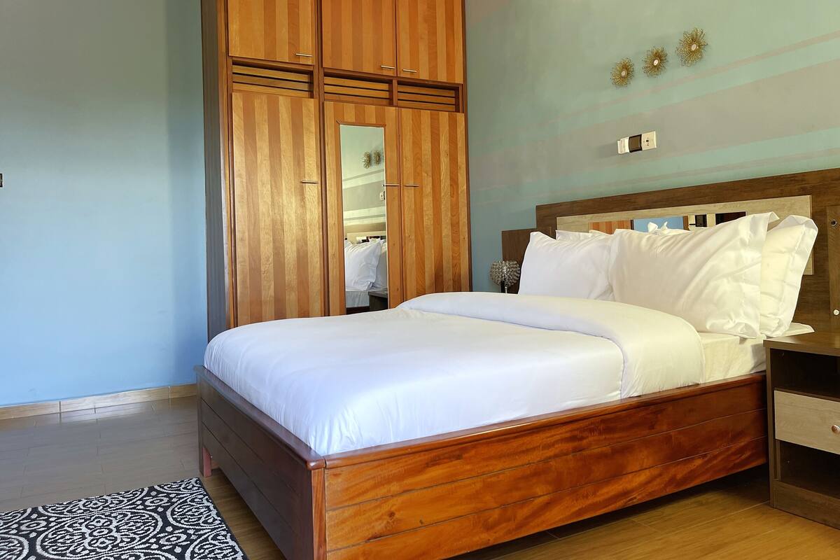 Una cama bien tendida con sábanas blancas, cabecera de madera y un amplio armario con espejo.