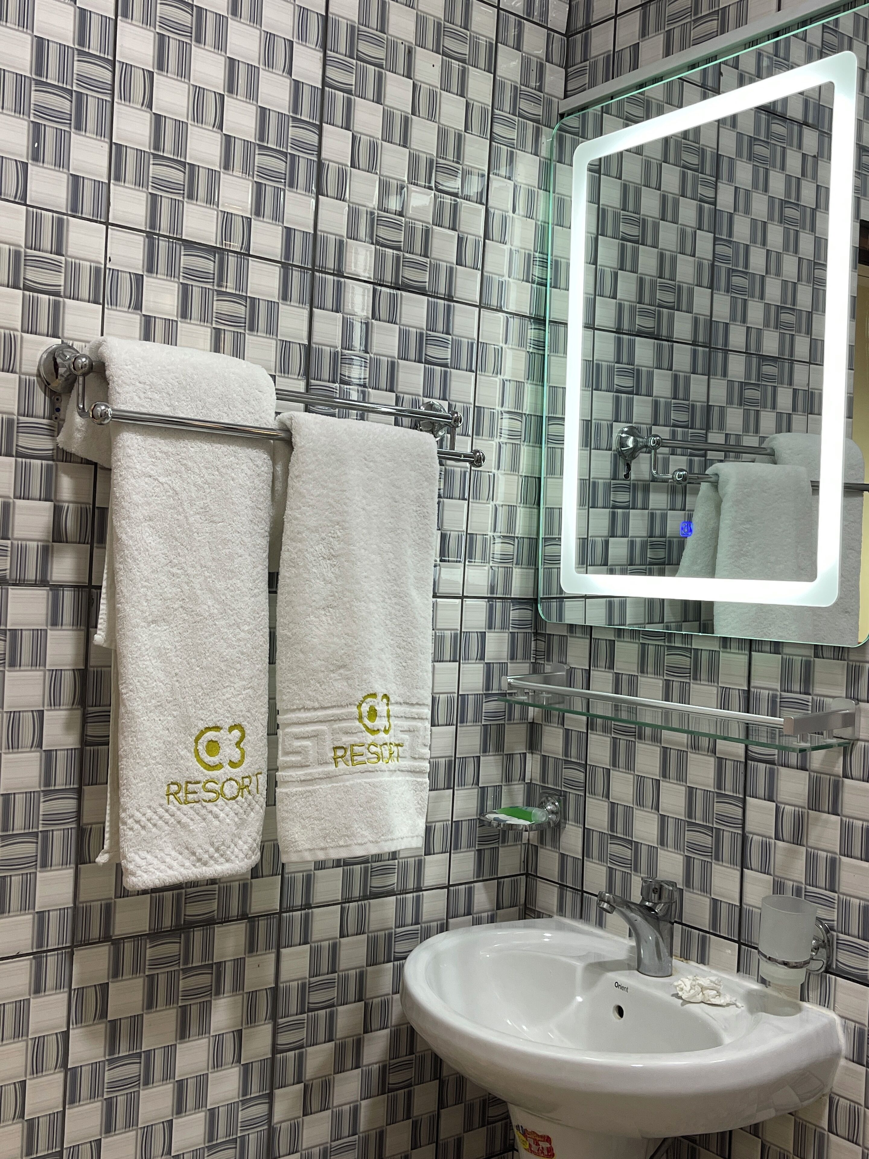 A bathroom with striped tile walls, a white sink, and two towels hanging on a towel rack with "RESORT" embroidered on them.