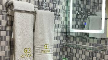 A bathroom with striped tile walls, a white sink, and two towels hanging on a towel rack with "RESORT" embroidered on them.