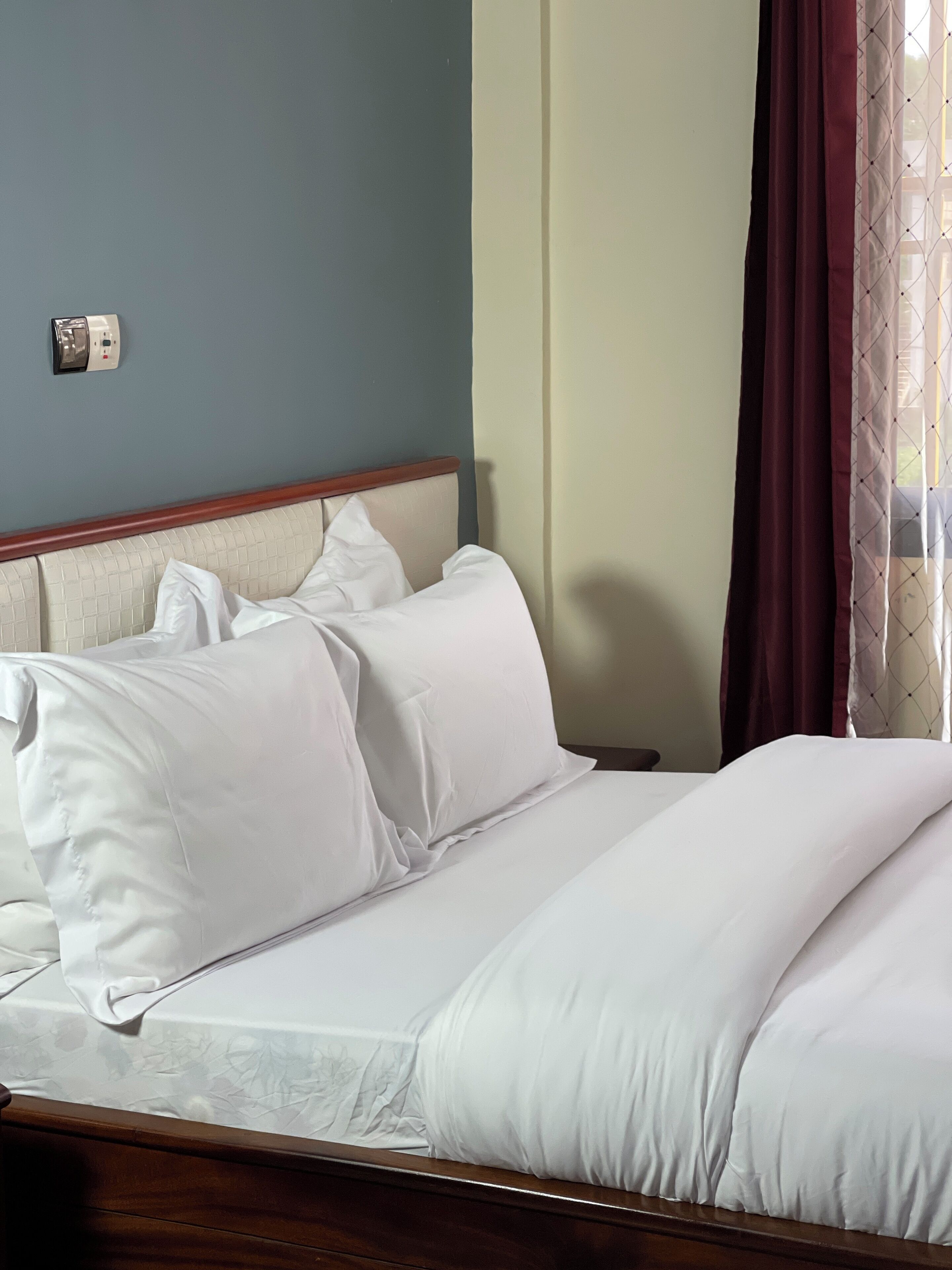 A neatly made bed with white linens in a room with a blue wall and a wooden headboard.