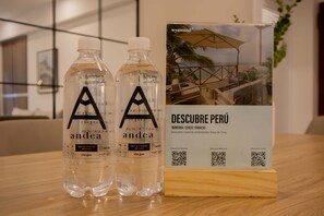 Two bottles of water labeled 'andea' and a brochure titled 'DESCUBRE PERÚ' with QR codes for 'Descubre Paracas', 'Descubre Máncora', and 'Descubre Cusco'.