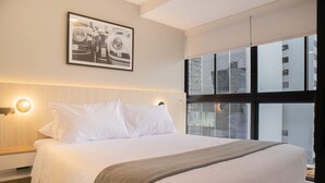 A modern hotel room with a large bed, a framed picture on the wall, and a view of a building through the window. - Incredible 2BR With Balcony in San Isidro (Lima)