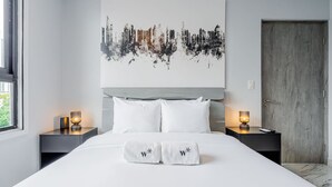Een moderne hotelkamer met een groot bed, witte beddengoed, twee nachtkastjes met lampen en een stadsgezichtschilderij aan de muur.