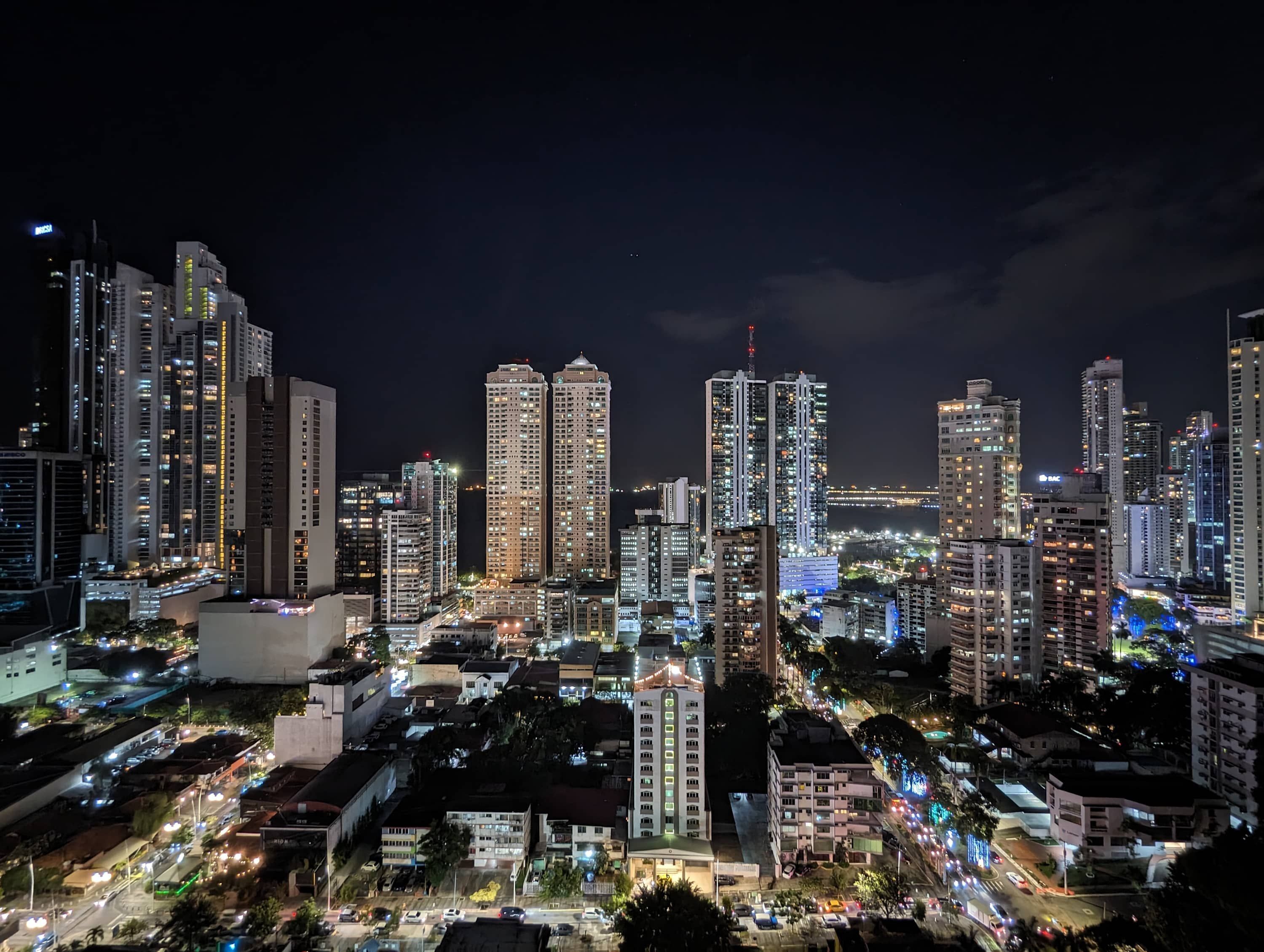 A nighttime cityscape with high-rise buildings, busy streets, and illuminated windows.