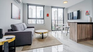 Een moderne woonkamer met een grijze bank, een ronde salontafel en een aan de muur bevestigde televisie.