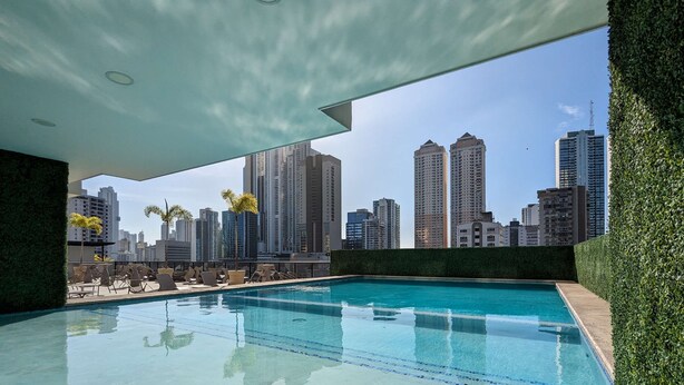Piscina no terraço com vista para o horizonte da cidade, cercada por vegetação e arquitetura moderna.