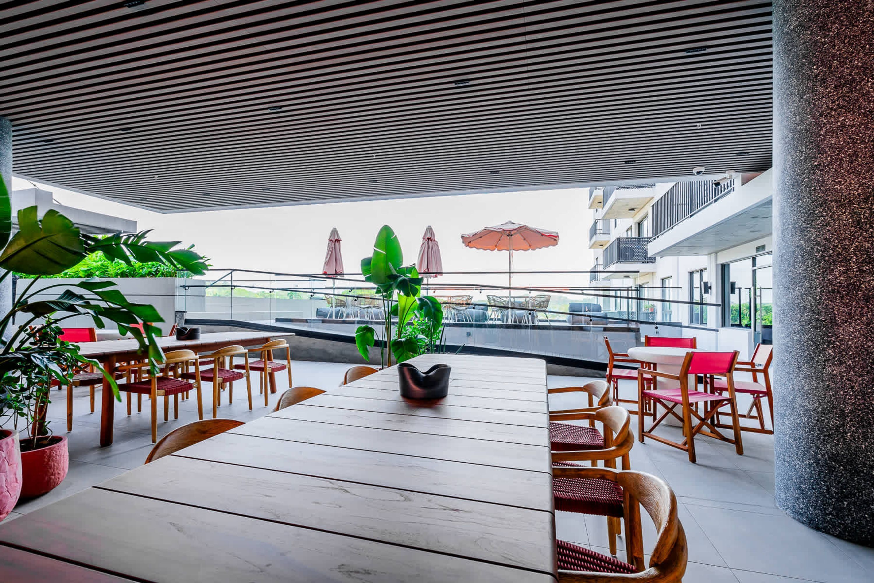 An outdoor dining area with wooden tables and chairs, potted plants, and umbrellas.
