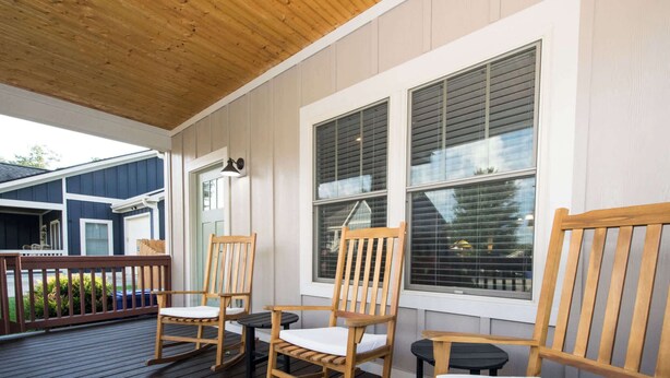 Une terrasse en bois avec des fauteuils à bascule et une table, donnant sur un quartier résidentiel.