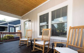 Um deck de madeira com cadeiras de balanço e uma mesa, com vista para uma área residencial.