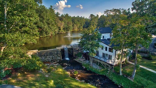 Une maison avec un étang, une cascade et une végétation luxuriante.