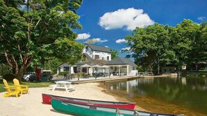 Une propriété au bord du lac, comprenant une maison, une plage de sable et des canoës.