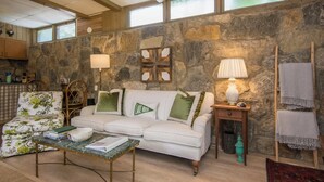 Un salon chaleureux avec un mur en pierre, un canapé blanc, une table basse en bois et une cheminée.