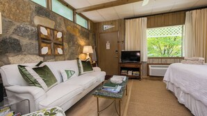 Une pièce chaleureuse avec un mur en pierre, un canapé blanc, une télévision, un lit et une fenêtre avec des rideaux.