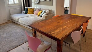 Een moderne woonkamer met een houten eettafel, een bank met kleurrijke kussens, en een groot bord waarop 'gut' staat.