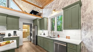 A modern kitchen with green cabinets, a stainless steel refrigerator, and a large window overlooking greenery.
