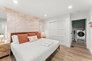 Un dormitorio con una cama grande, una mesita de noche, un espejo, un armario y un área de lavandería.
