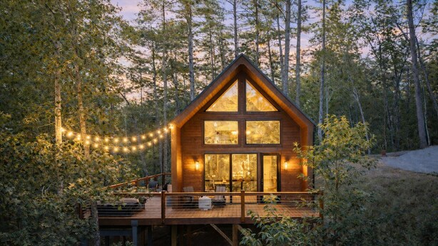 A wooden cabin with a deck, surrounded by trees.
