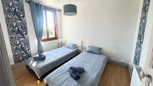 A bedroom with two beds, a window with curtains, a hanging light fixture, and a radiator.