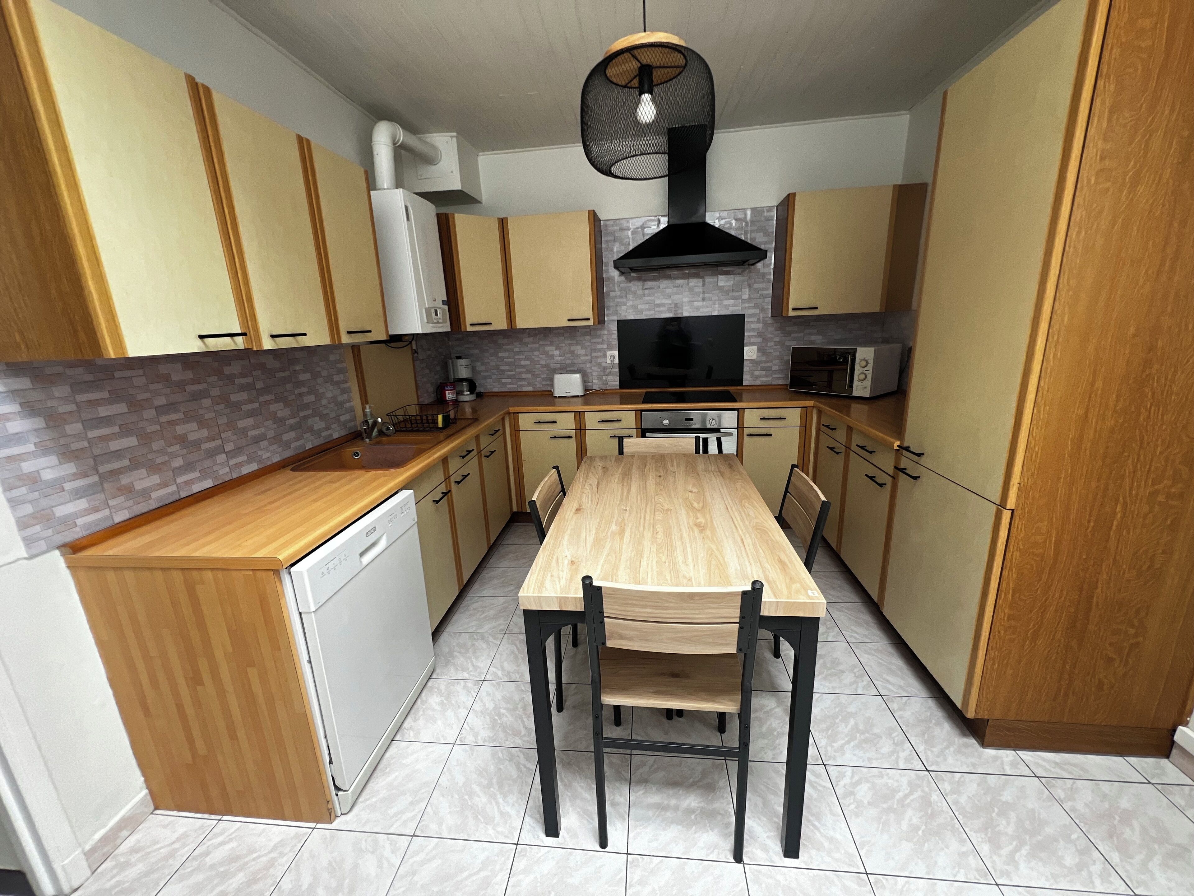 A compact kitchen with wooden cabinets, a built-in oven, a microwave, and a dining table with chairs.
