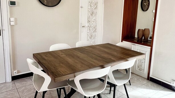 A dining area with a wooden table, white chairs, a world map clock, and a mirror on the wall.