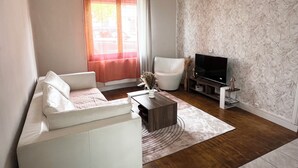 A living room with a sofa, a coffee table, a TV on a stand, and a patterned wallpaper.