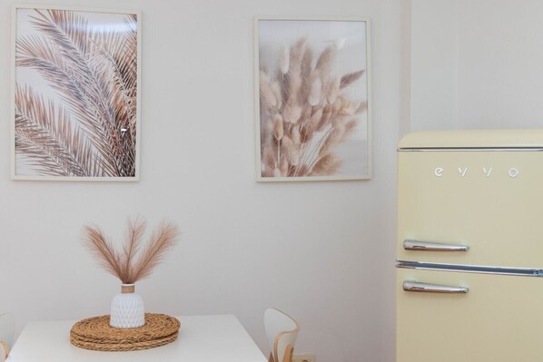 A dining area with a table, chairs, a vase with dried pampas grass, and a vintage-style refrigerator.