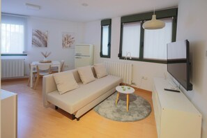 A modern living room with a sofa, a small round table, a TV, and a radiator.