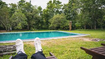 A poolside view with a wooden deck and a pool surrounded by trees.