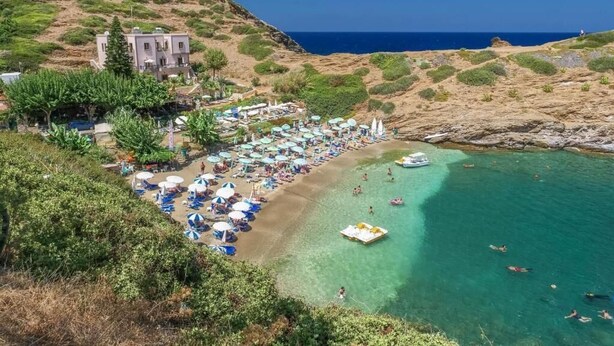 Un complejo turístico en la costa con playa, sombrillas y un edificio.