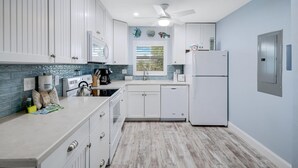 A modern kitchen with white cabinets, a built-in oven, a refrigerator, and a window with blinds. - Seashells #45-Sanibel Condo with Gulf Access! (Sanibel)