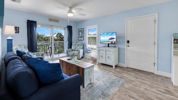 A living room with a sofa, a coffee table, a TV, a ceiling fan, and a view of the outdoors. - Seashells #45-Sanibel Condo with Gulf Access! (Sanibel)