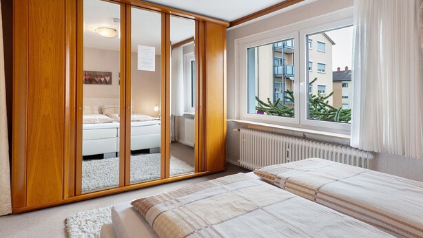 Un dormitorio con un armario grande, una cama, un ventanal con vistas a edificios y un radiador.