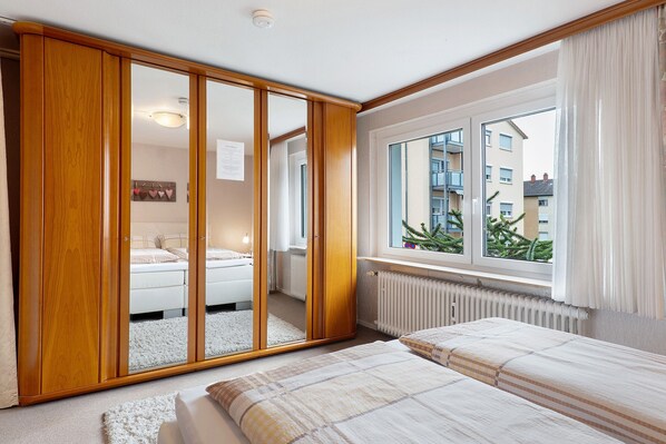 Ein Schlafzimmer mit großem Kleiderschrank, einem Bett, einem Fenster mit Blick auf Gebäude und einer Heizung.