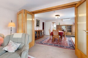 Ein Wohnzimmer mit einer Couch, einem Esstisch mit Stühlen, einem gemusterten Teppich und Holzkredänzen.
