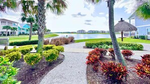 A landscaped area with palm trees, a pathway, and a view of a body of water and buildings in the background. - The Flamingo Nest - Kid Friendly (Kissimmee)