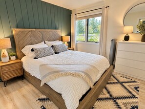 A bedroom with a wooden bed, bedside lamps, a window with a view, and a mirror.