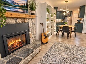 A modern living room with a fireplace, a dining area, and a kitchen with teal cabinetry. - Updated Ski-In/Ski-Out Condo | Hot Tub & Pool (Lutsen)