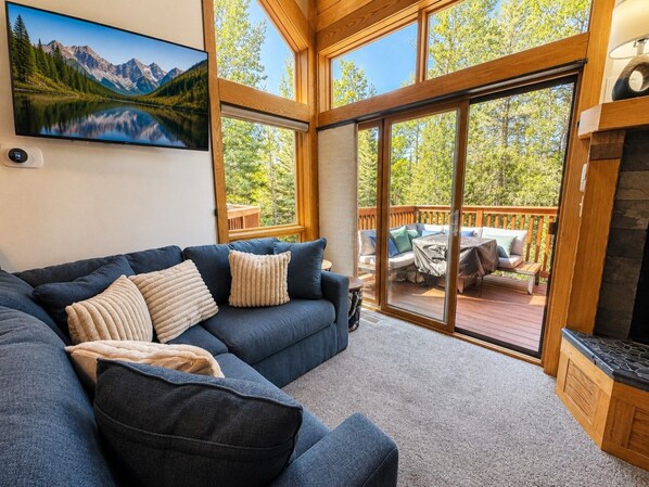 A cozy living area with a sectional sofa, a fireplace, and a large window overlooking a deck.