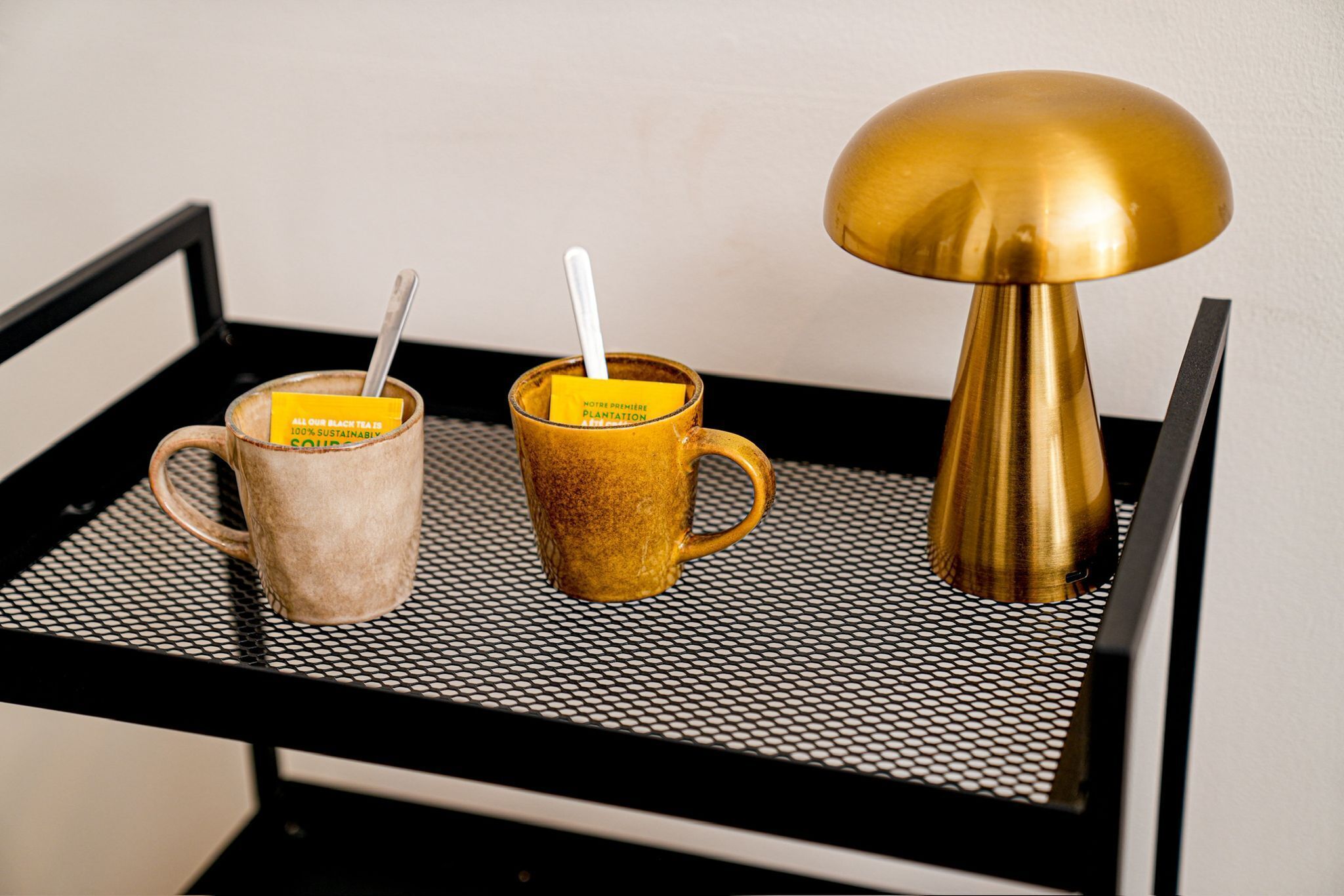 Two coffee cups on a black metal tray with a gold-colored lamp beside them.