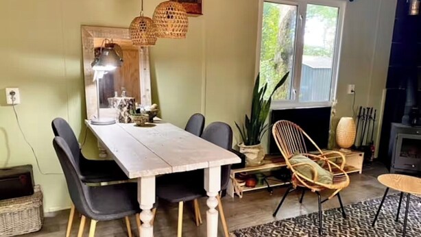 Un espace repas comprenant une table en bois, des chaises noires, des chaises en osier et des lampes en osier suspendues au plafond.