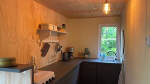 Une cuisine compacte aux murs en bois, dotée d’une cuisinière intégrée, d’une machine à café et d’une fenêtre donnant sur un paysage verdoyant.