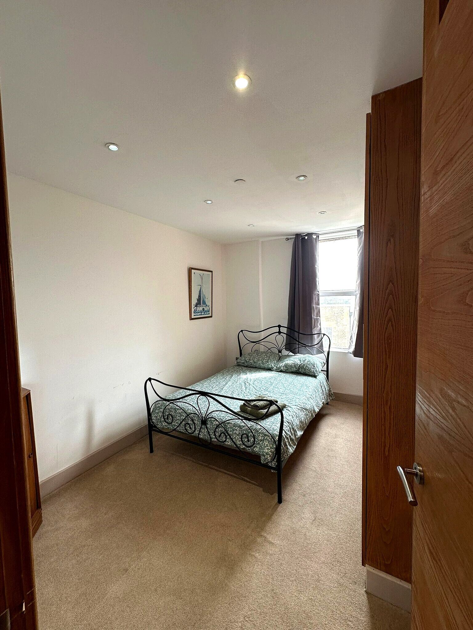 A bedroom with a single bed, a window with curtains, and a door.