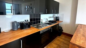 Une cuisine moderne avec des meubles de couleur noire, un plan de travail en bois et des appareils électroménagers en acier inoxydable.