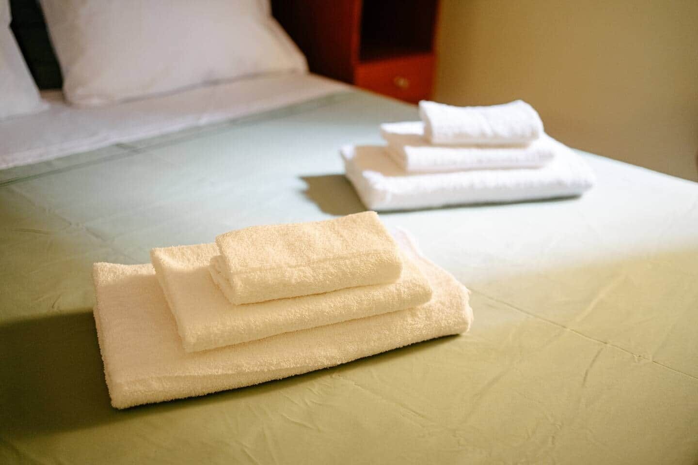 Cama com toalhas brancas bem dobradas e um cobreleito simples.