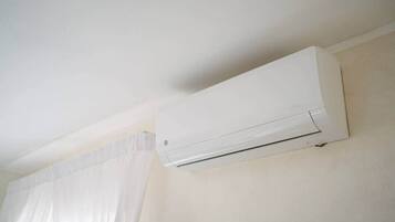 A white air conditioning unit mounted on a wall in a room with a window and curtains.