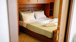 Una cama con almohadas blancas y colcha verde, cabecero de madera y armario de madera arriba.